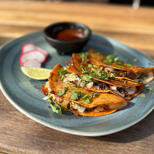 Three crispy tacos and a small bowl of sauce on a blue plate.