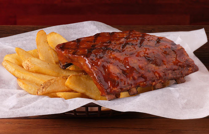 Ribs and fries on white parchment in a black wire tray.