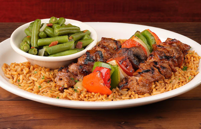 Rice, meat kabobs, a veggie kabob, and a bowl of beans, all on a white plate.