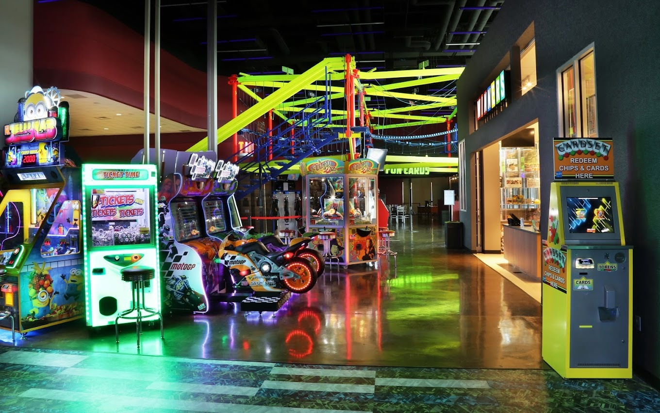 An view of a large arcade room, dimly lit with lots of glowing arcade games filling the room.