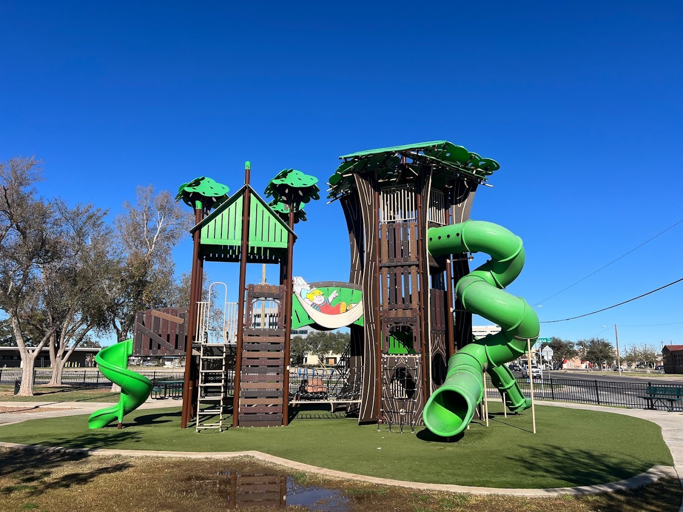 An outside view of a large green and dark brown playground with many large green slides.
