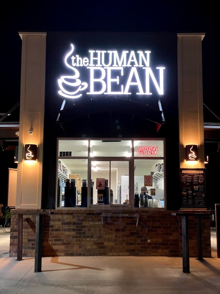 An store lit up at night with a white sign illuminating reading "The Human Bean" above the entrance.