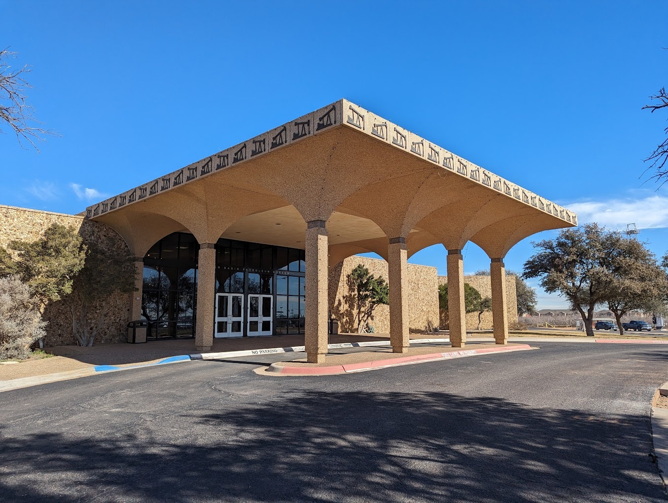 An outside view of a light beige building with a large awning covering a drive up approach attached to the driveway.