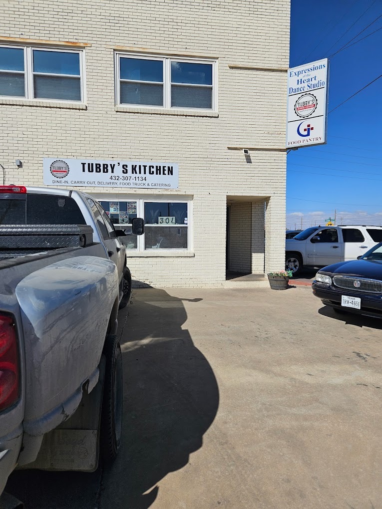 A view of a white building with many windows and a white sign above the windows and to the left of the door "Tubby's Kitchen"