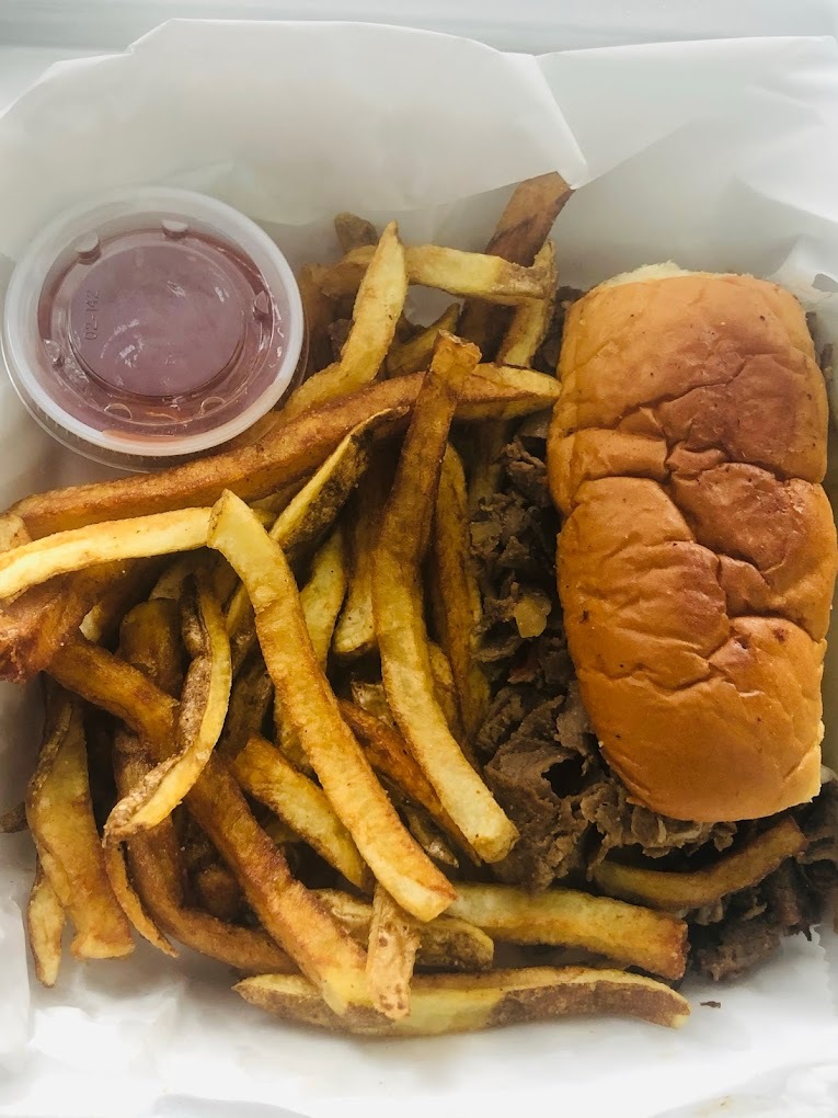 A to go box filled with homestyle classic cut fries, and a large burger with a side of sauce.