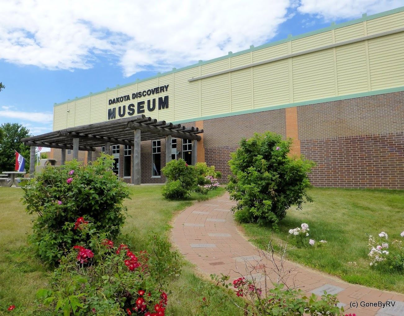 Dakota Discovery Museum entrance, sidewalk lined with flowers and shrubbery.