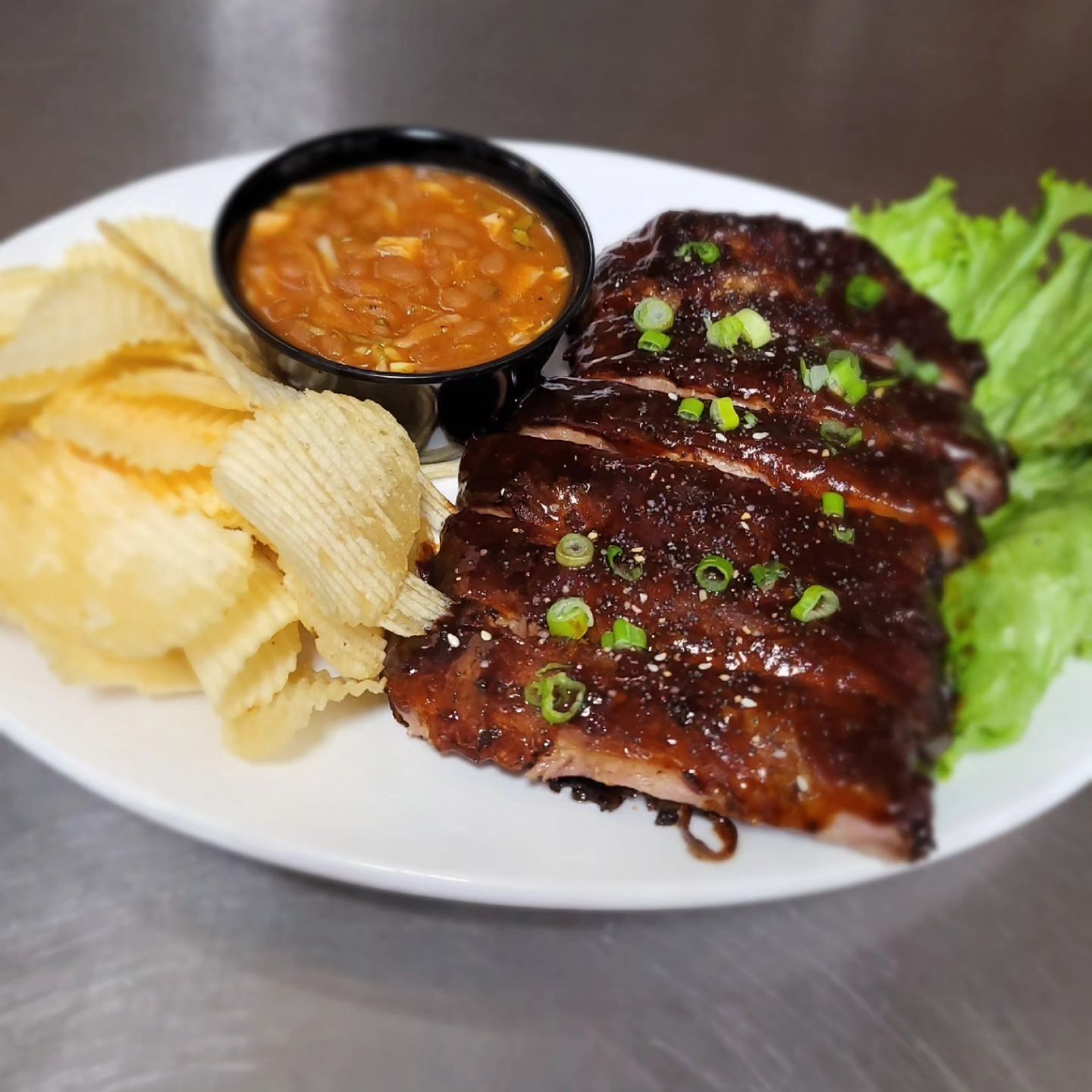 White plate with ribs, chips, and a side of lettuce with a side of soup.