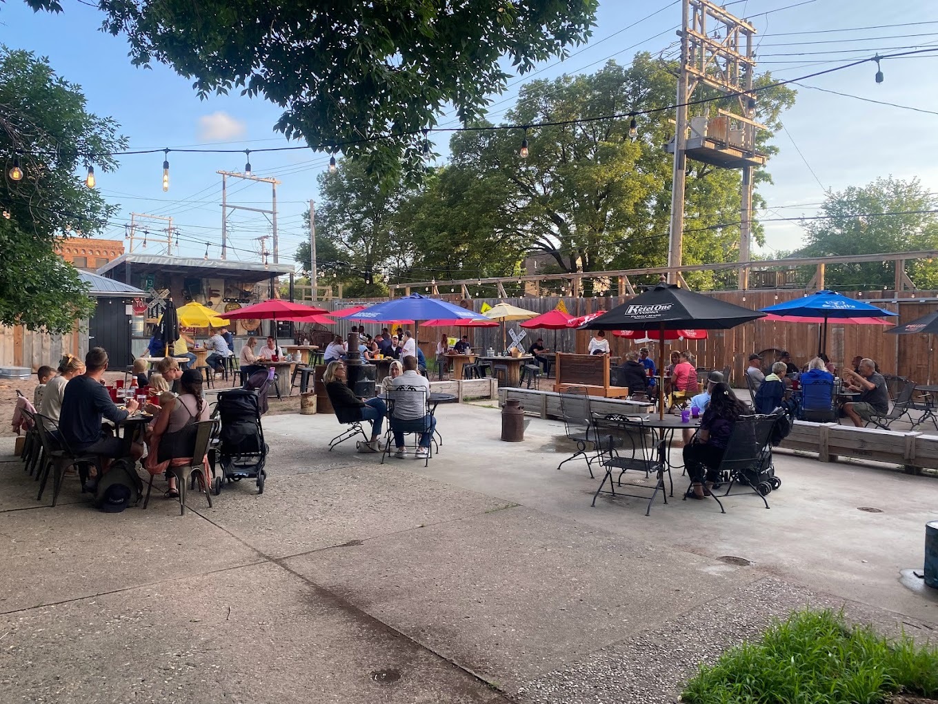Patio full of patrons sitting on tables and chairs covered by umbrellas.