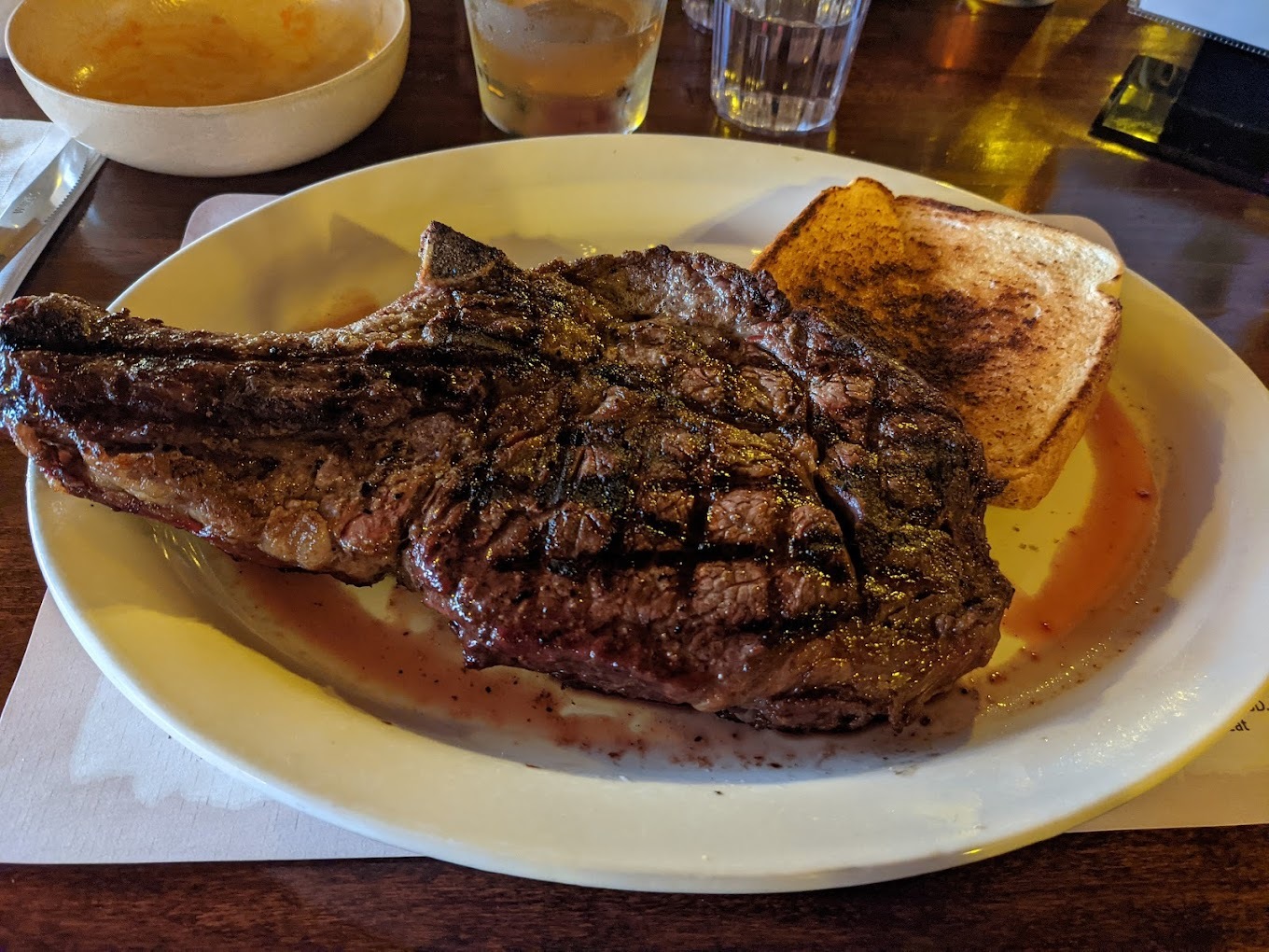 A very large steak that is served on a white plate also served with a side of toast.