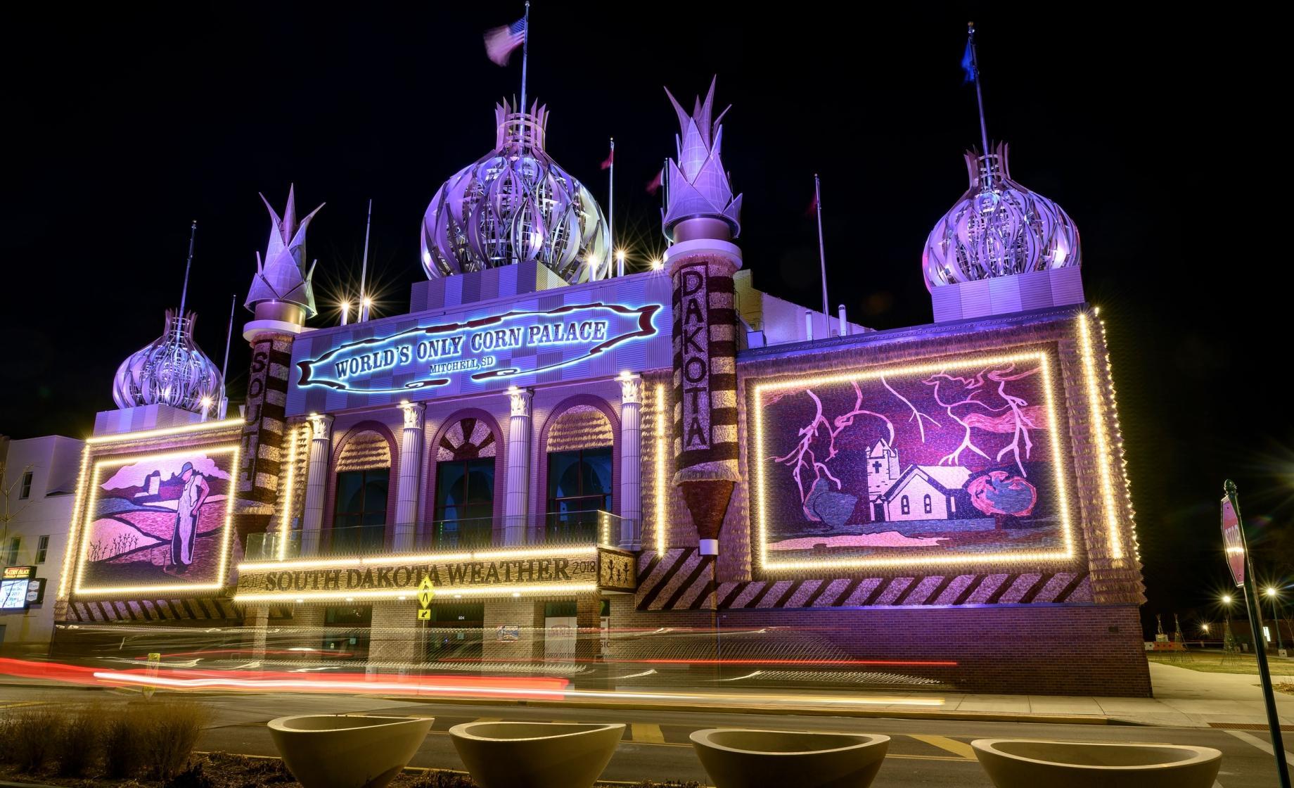 Large palace building light up with blue and purple lights. Illustrative corn images on the wall of the palace.