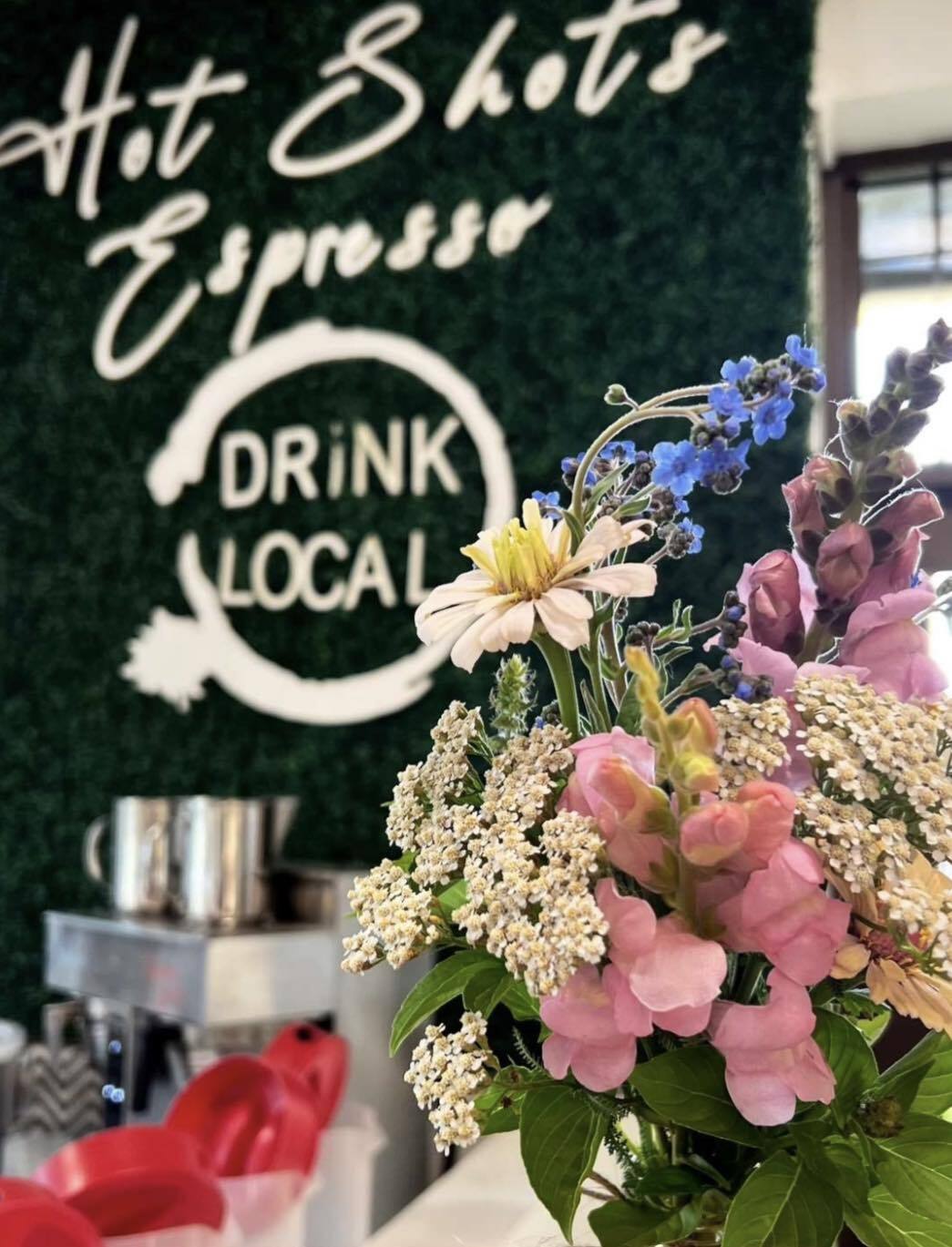 An view of an espresso bar with machines on the counter and a bouquet of flowers on the counter.