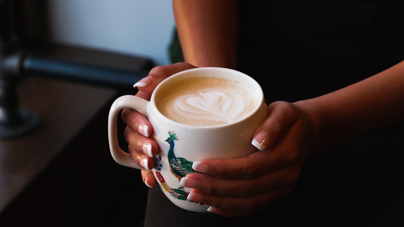 Women with a french manicure holding a warm coffee with a cream heart latte art.