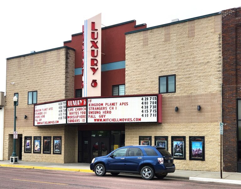 An old school theatre entrance vertical signage reading "Luxury 5" with a blue car in front.