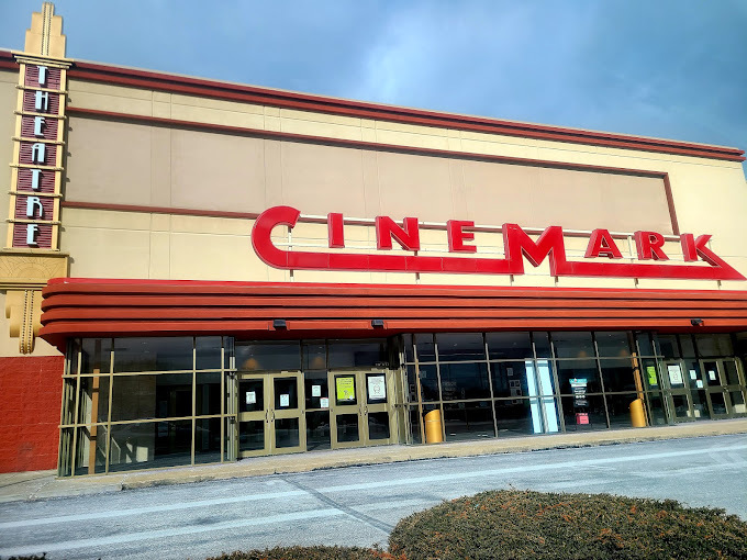 Large flat beige building. There is a strip of red above the door and window entrance, with a sign above that saying "Cinemark." Off to the left side is a vertical sign that says "theatre."