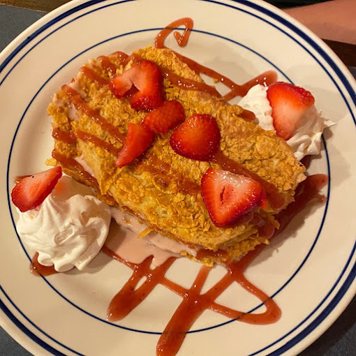 French toast with strawberries, strawberry sauce, and whipped cream. This is set on a white plate with blue accents.