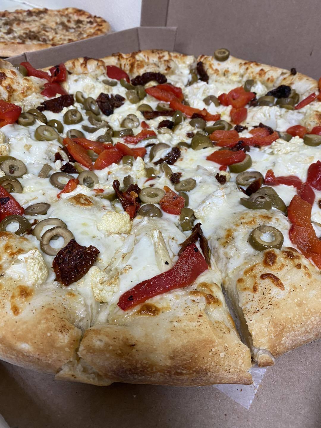 Up close view of fluffy pizza with olives, peppers, and cheese.
