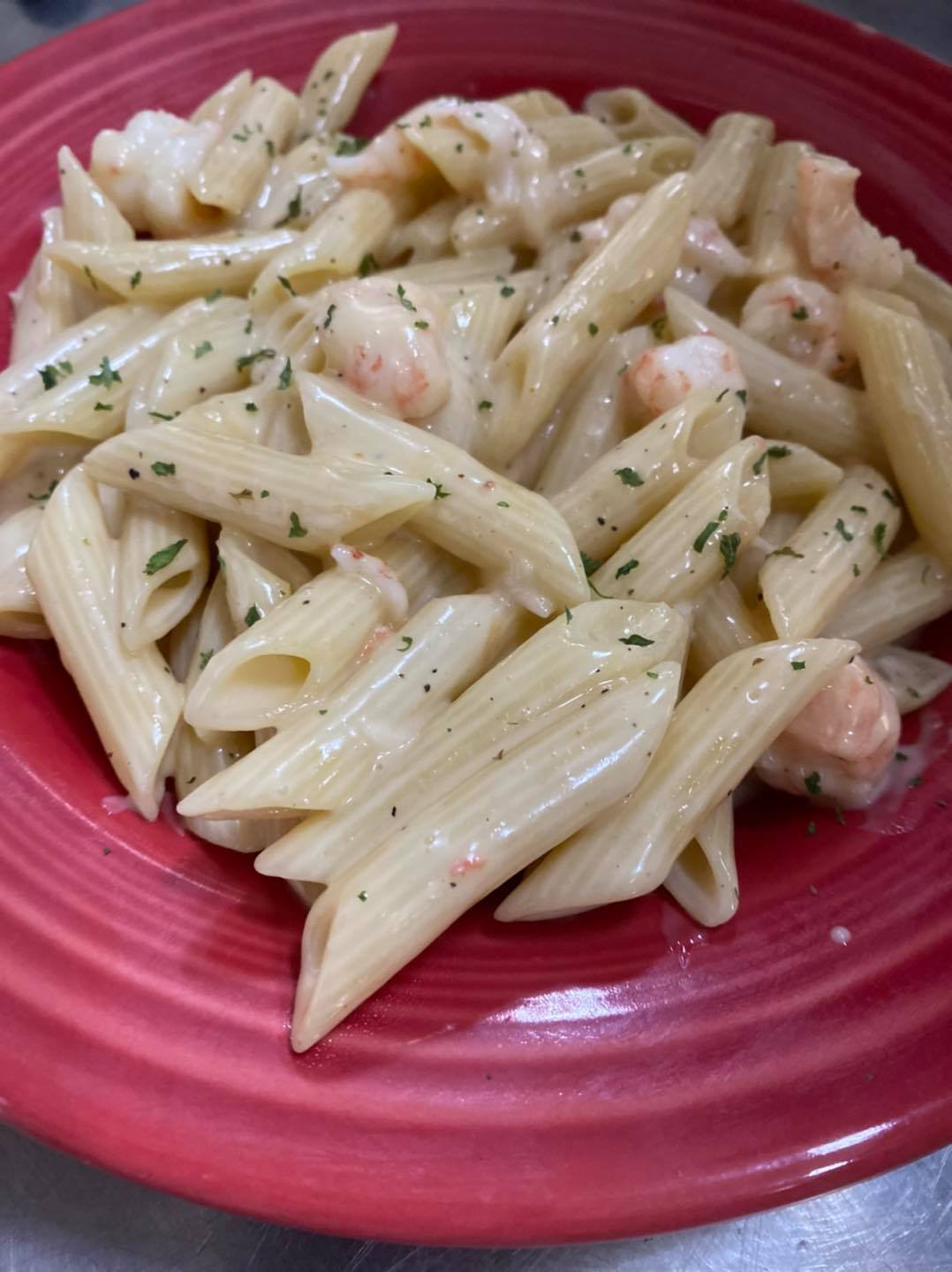 Penne noodles with sauce, seasonings, and shrimp. This dish is on a red plate.