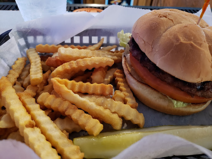 A basket with paper serving up a large burger and crinkle cut French fries.