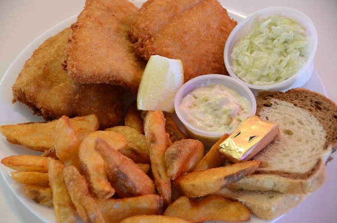 A white plate consisting of a meal of chicken wings, fries, and bread with butter and two containers of sauce on the side.