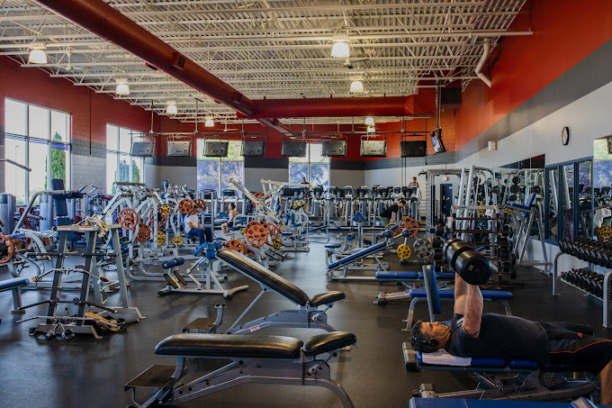 An indoor view of an gym filled with work out equipment, the ceiling of the room is white and an orange border surrounds the top of the walls.