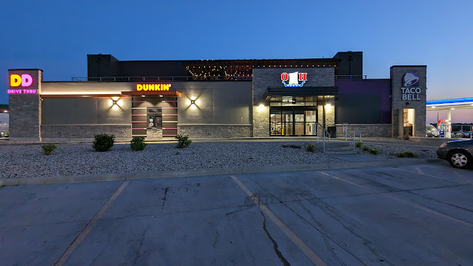 An outdoor view of a coffeeshop at night, a small building with a sign on the side for Dunkin and the Drive thru.