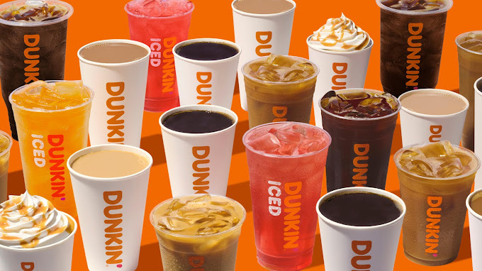 A view of a large grouping of different kinds of hot and cold Dunkin Donuts drinks on an orange background.