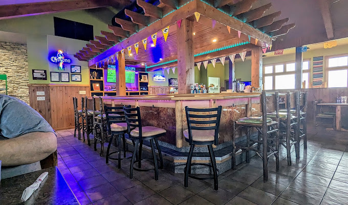 An inside view of a bar with an awning above the bar, lights illuminate the top of the bar blue, and flags decorate the top of the bar.