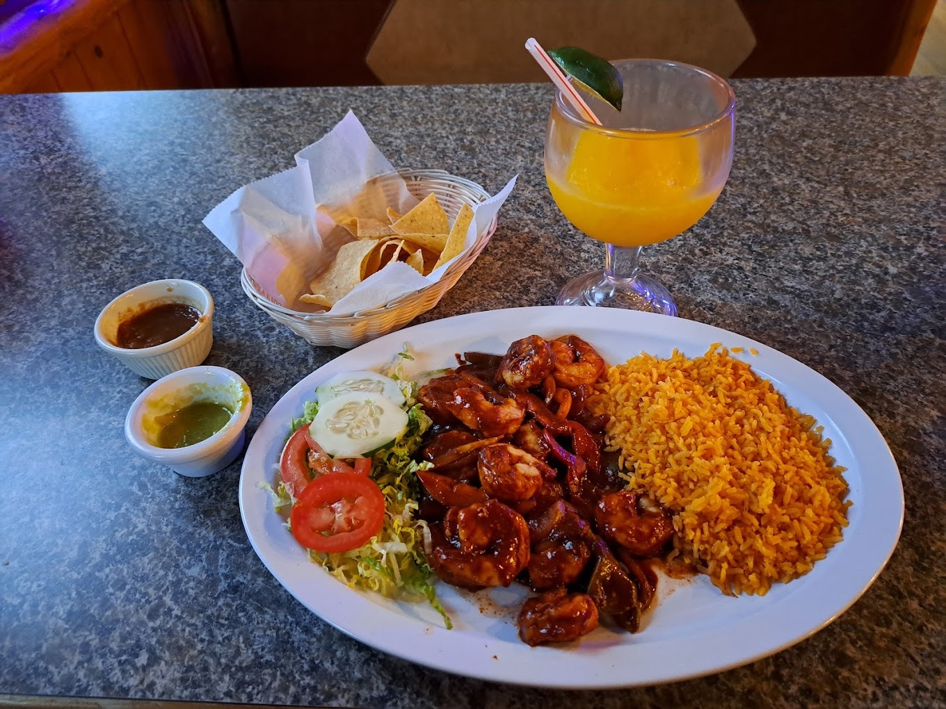 A large white plate with shrimp, a side of fried rice, and a side salad. Another basket full of chips and two sides of sauce with a margarita to drink!