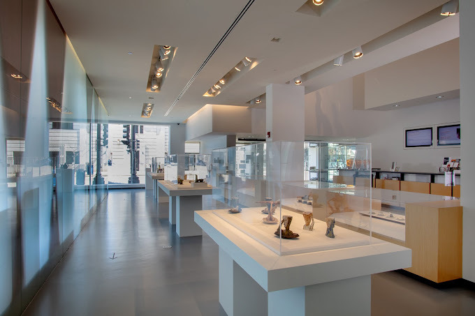 An indoor view of a very white filled room. Tables and shelves in the room are filled with pieces of art.