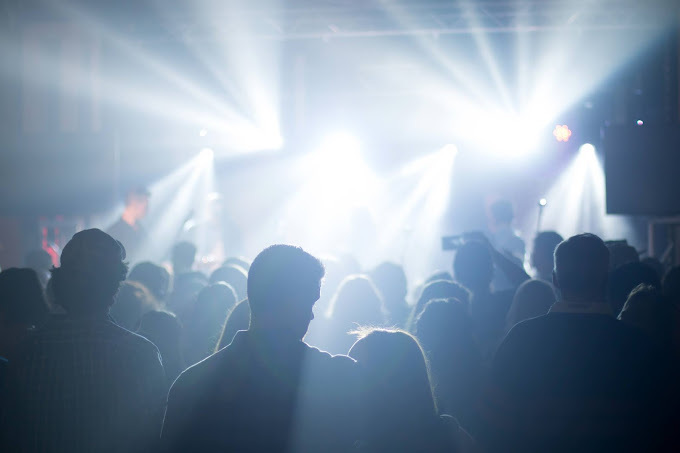 A view of a crowd of concert goers in a dark room, only lights coming from the front of the room.