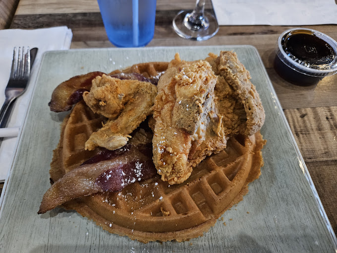 A view of a metal serving dish with a large Belgium waffle topped with syrup, bacon and fried chicken.