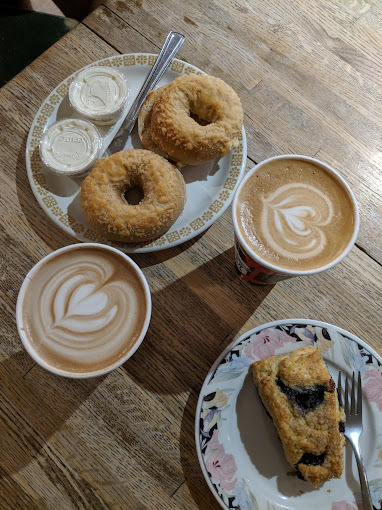 Overhead view of two foam art hot coffees, a plate of two doughnuts, and a plate with a baked good.