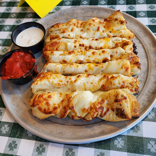 Cheesy breadsticks and two sauces on a plate with a green gingham pattern underneath.