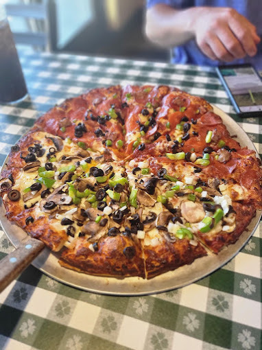Close view of a pizza with divided toppings on a green pattern table cover.