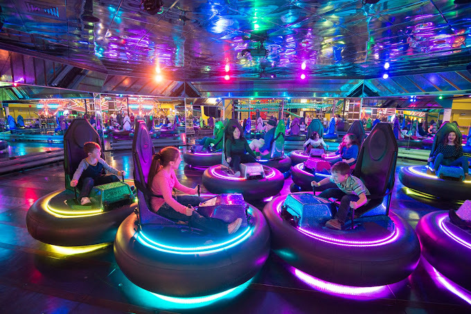 Dark lit image of neon glowing bumper karts with numerous children.