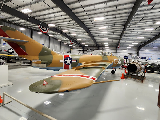 Side view of a orange and green airplane inside a garage type building.