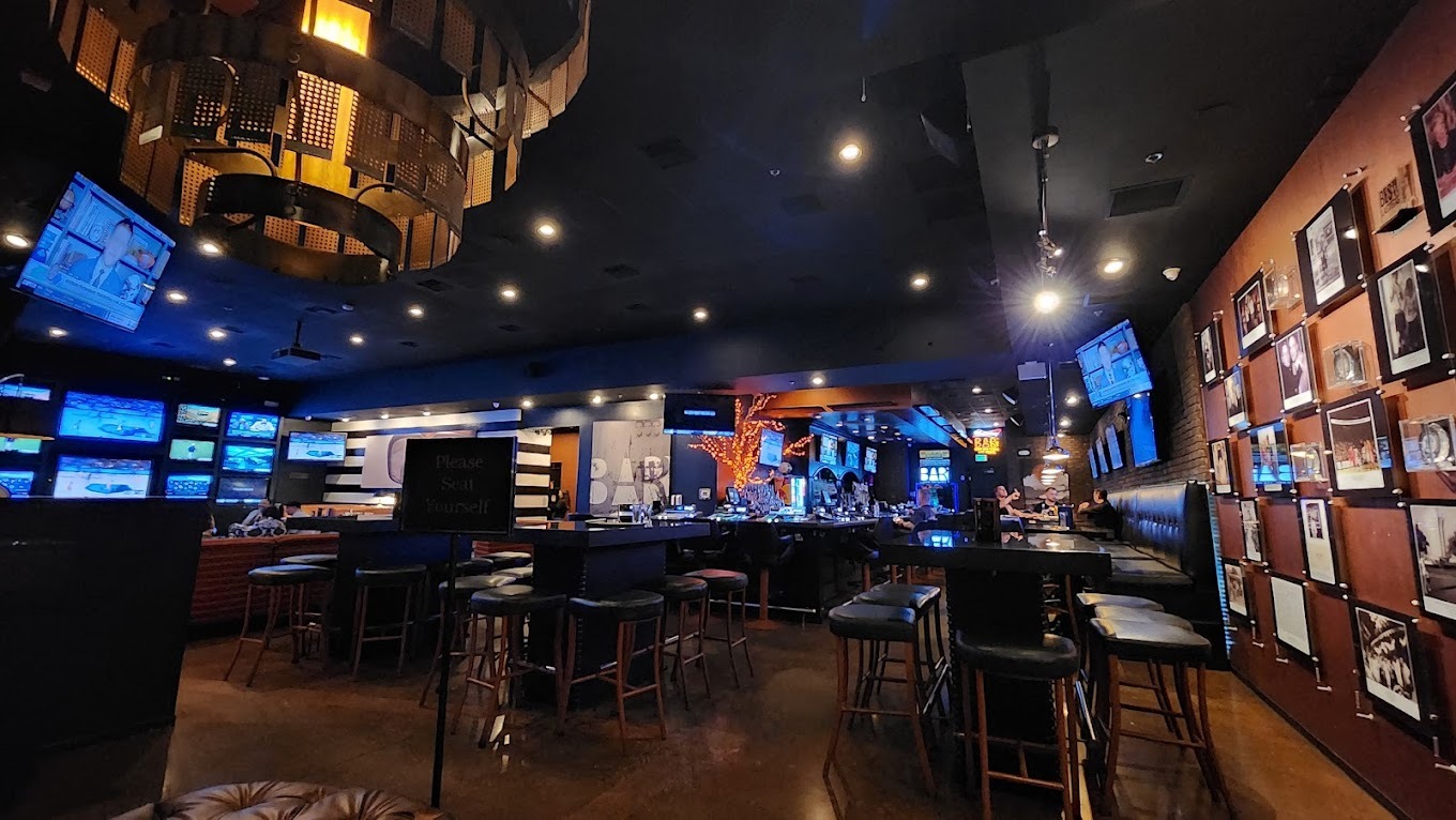 An inside view of a social bar, large chandeliers on the ceiling along with many TV's lining the wall.
