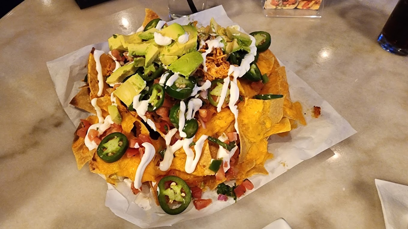 A photo of nachos topped with sour cream, cheese, jalapenos, avocado, onion, and green garnish.