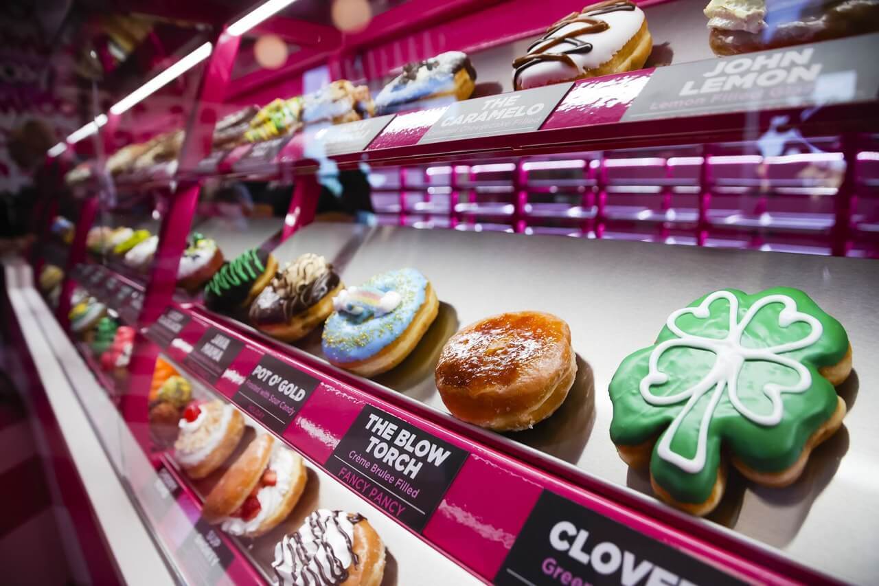 A close up view of a display case full of doughnuts, featuring specialty donuts including a shamrock.