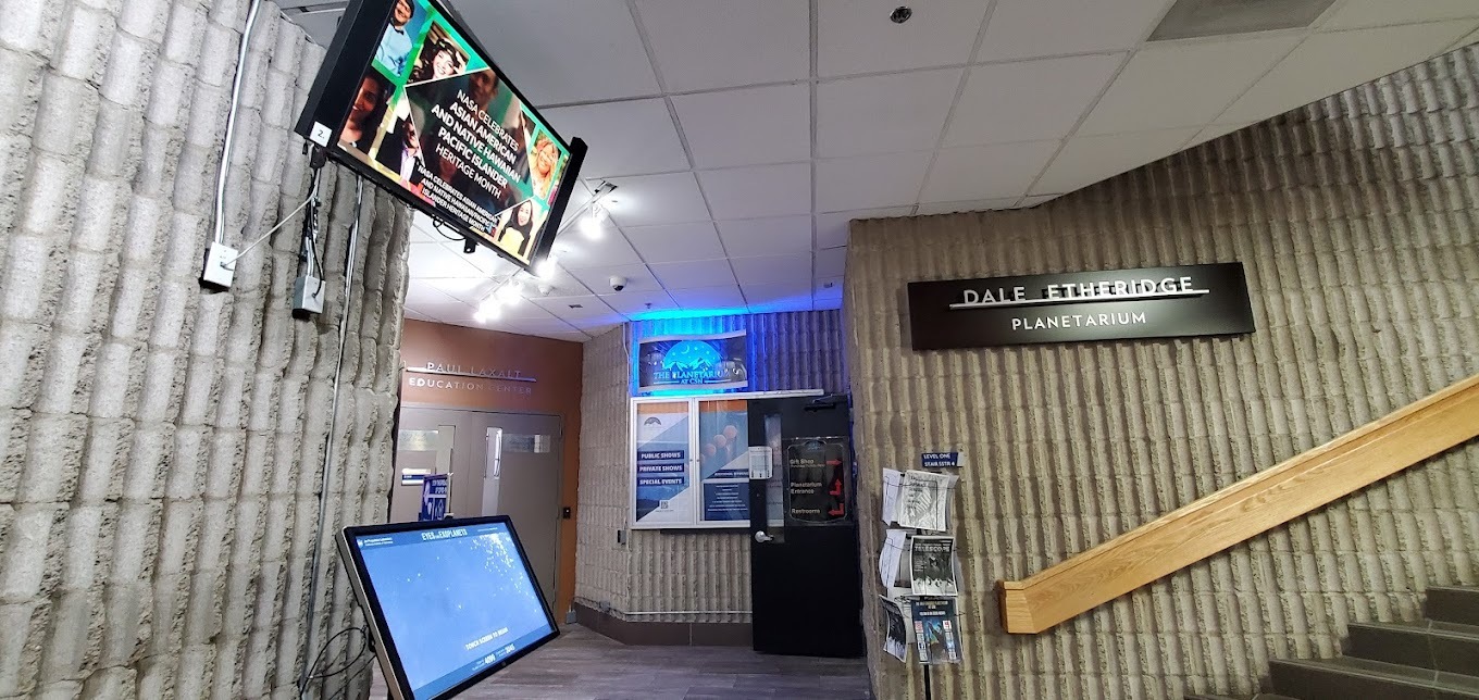 A view of the entrance to the Planetarium, a beige colored walkway with tv's showing information.