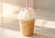 Creamy iced coffee topped with whipped cream in a clear plastic cup with a bright pink straw on a clean, softly lit surface.