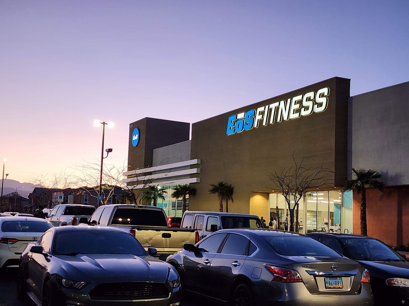 A brown and white colored modern style building with a large white and blue sign reading "Eos Fitness"