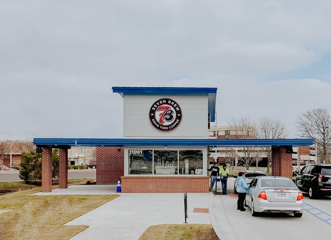 A white, brick and blue building with a drive thru awning. Round shaped signage reading "7 Brew Coffee"