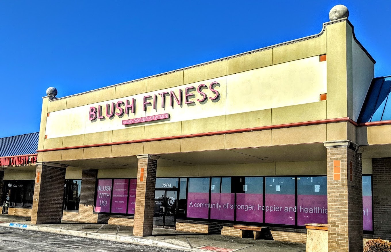 A light tan building with pink window covers, the sign above the door reads "Blush Fitness" in pink lettering.