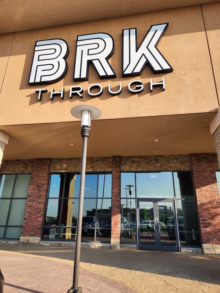 An entrance to a retail space, dark tan building with a white sign above the doors reading "BRKTHROUGH" in black and white.