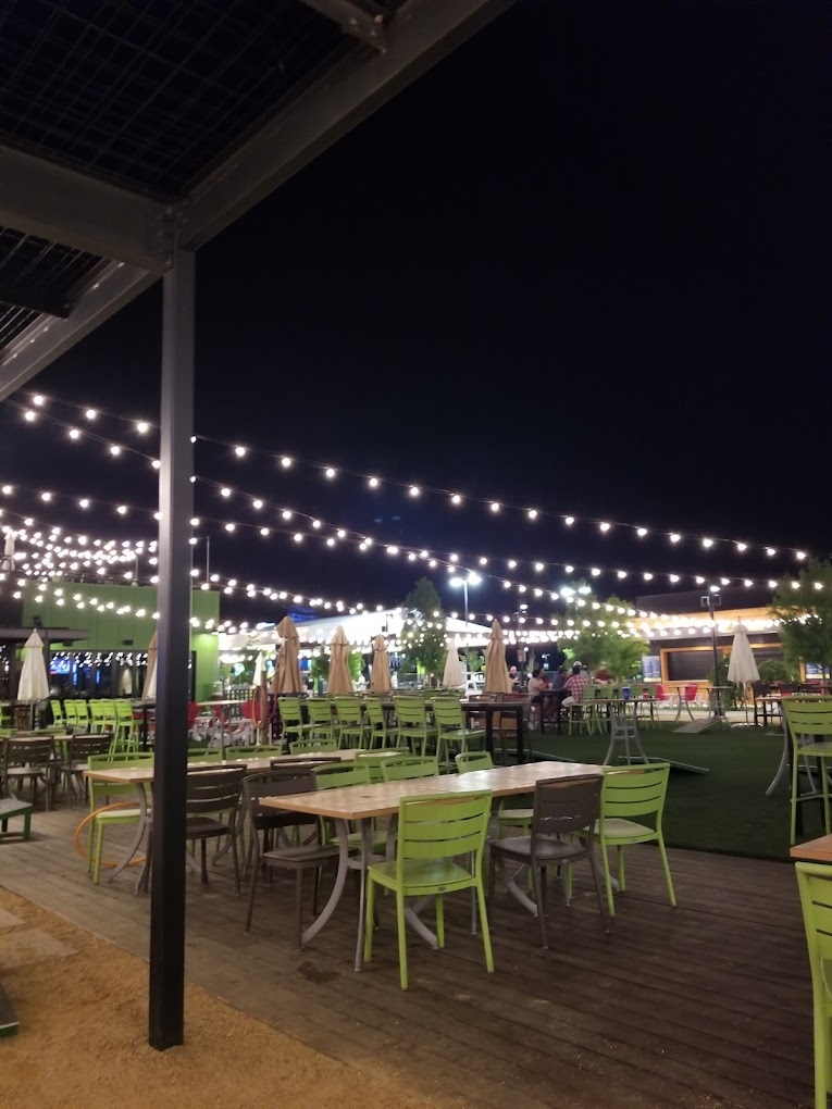 A night time view of a lighted patio dining area. White tables with light green chairs fill the area.