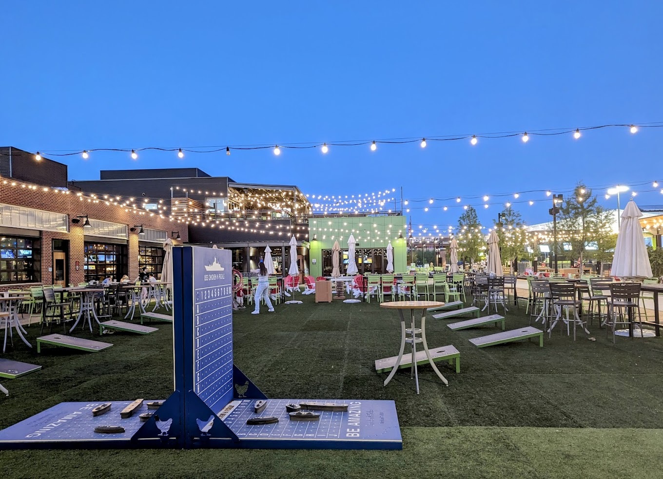 A large lighting outdoor game and seating area with light green accenting and many yard games.
