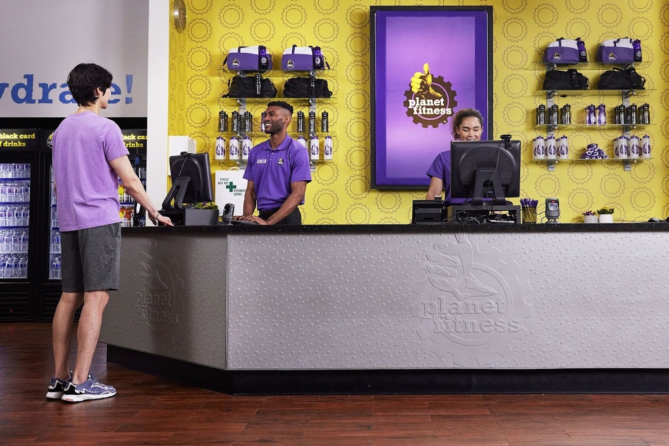 A front desk area with a yellow wall and purple signage. A man is being helped by a front desk employee.