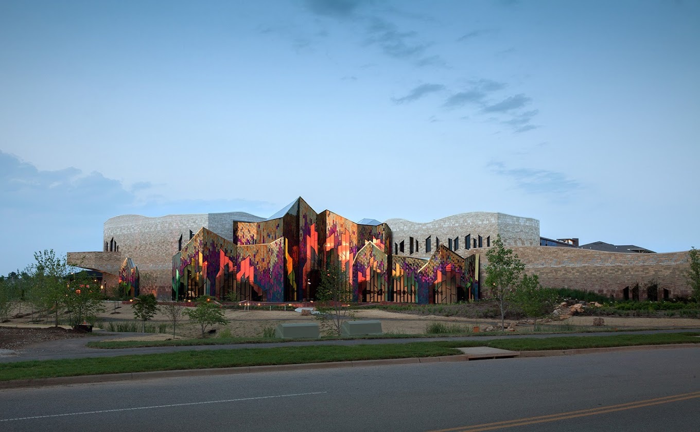 An far away view of the Prairie Fire Museum, the artwork of patchwork materials on the side of the building glows in the sunset.