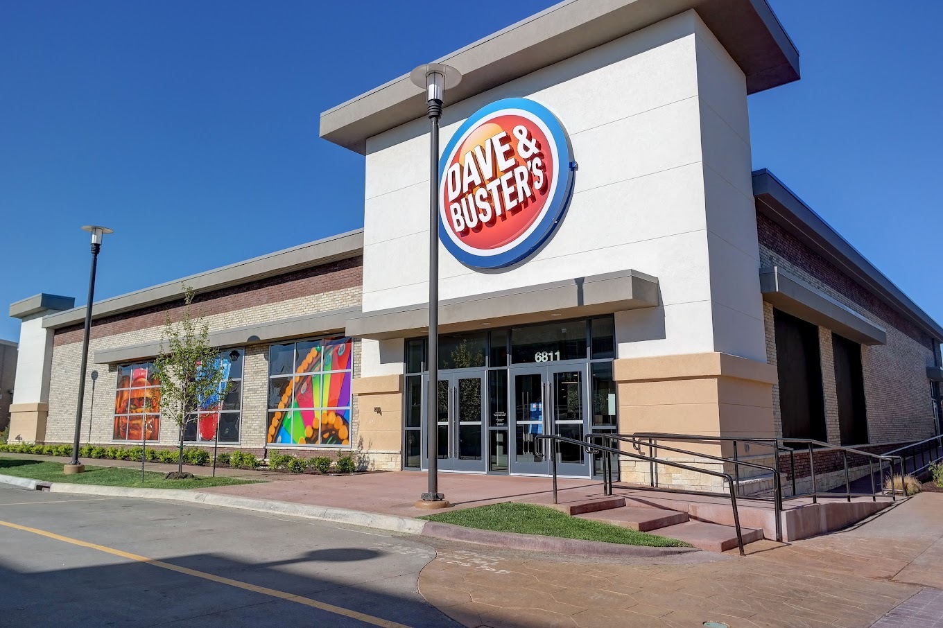 An outside view of Dave and Buster's, A large white and grey building with a large orange sign with a blue and white outline reading "Dave and Buster's" in white lettering.